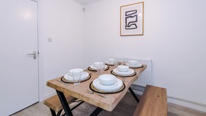 Ein Esstisch ist gedeckt mit weißen Tellern, Schüsseln und Besteck, an der Wand hängt ein gerahmtes, abstraktes Kunstwerk.