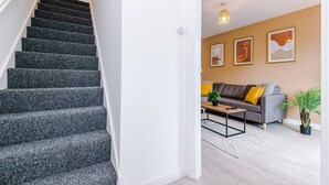 Eine Treppe mit dunklem Teppichbelag führt zu einem Wohnbereich mit Sofa, Couchtisch und Wandbildern.