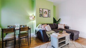 A living room with a green wall, a dark grey sofa, a dining table with chairs, and a lamp.