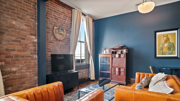 Un salon avec un mur en briques, un téléviseur, un meuble en bois et un canapé.