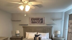Une chambre à coucher avec un grand lit, deux tables de chevet, un ventilateur de plafond et une étagère fixée au mur.