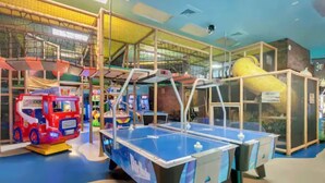 Un espace de jeux intérieur avec une table de ping-pong bleue, une voiture jouet rouge et une structure d’escalade jaune.