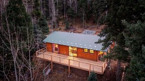 A cabin with a metal roof, wooden deck, and large windows. - Remodeled Cabin Chic 2BR, Solar in Taos Canyon — unplug, unwind, and enjoy. (Taos)