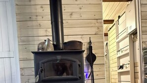 A wood-burning stove in a room with wooden walls and a rug. - Remodeled Cabin Chic 2BR, Solar in Taos Canyon — unplug, unwind, and enjoy. (Taos)