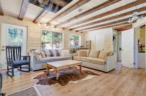 A room with wooden beams, a sofa, a rocking chair, and a cowhide rug.