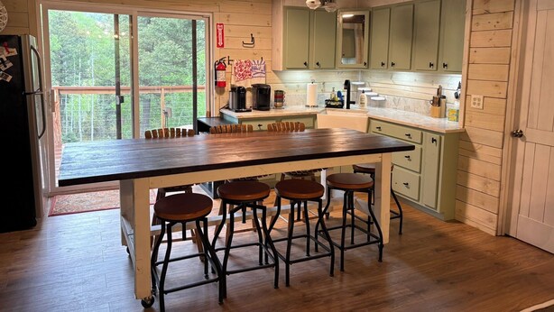 A kitchen with a large island, bar stools, wooden cabinets, and a view of greenery outside. - Remodeled Cabin Chic 2BR, Solar in Taos Canyon — unplug, unwind, and enjoy. (Taos)