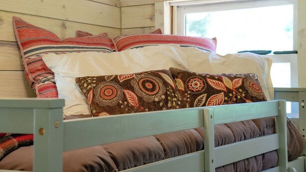 A wooden cabin interior with a bed featuring multiple pillows and a window. - Remodeled Cabin Chic 2BR, Solar in Taos Canyon — unplug, unwind, and enjoy. (Taos)