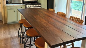 Una cocina con una mesa de madera y taburetes de bar, estufa, microondas, refrigerador y armarios.