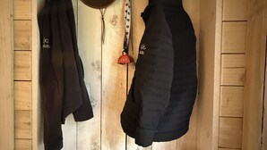 A wooden cabin interior with a coat rack holding two jackets, a hat, and a pair of gloves on a shelf. - Remodeled Cabin Chic 2BR, Solar in Taos Canyon — unplug, unwind, and enjoy. (Taos)