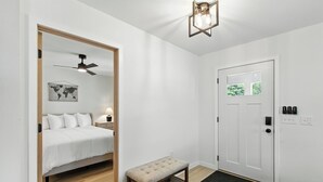 Habitación de hotel con cama, banco, mapa del mundo en la pared, ventilador de techo y puerta con ventanal.