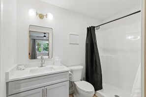 A bathroom with a white sink, mirror, toilet, and shower.