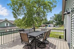 A wooden deck with a table and chairs, surrounded by a metal railing, overlooking a residential street.
