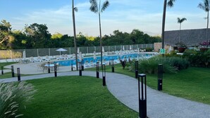 Un espace piscine agrémenté de chaises longues et de parasols, entouré d’une clôture et de verdure.