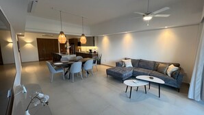 Un salon moderne avec un canapé gris, une table à manger avec des chaises, des luminaires suspendus et un ventilateur de plafond.