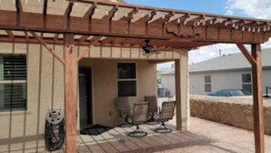 A covered patio with two chairs and a table, a ceiling fan, and a coiled cable on the ground.