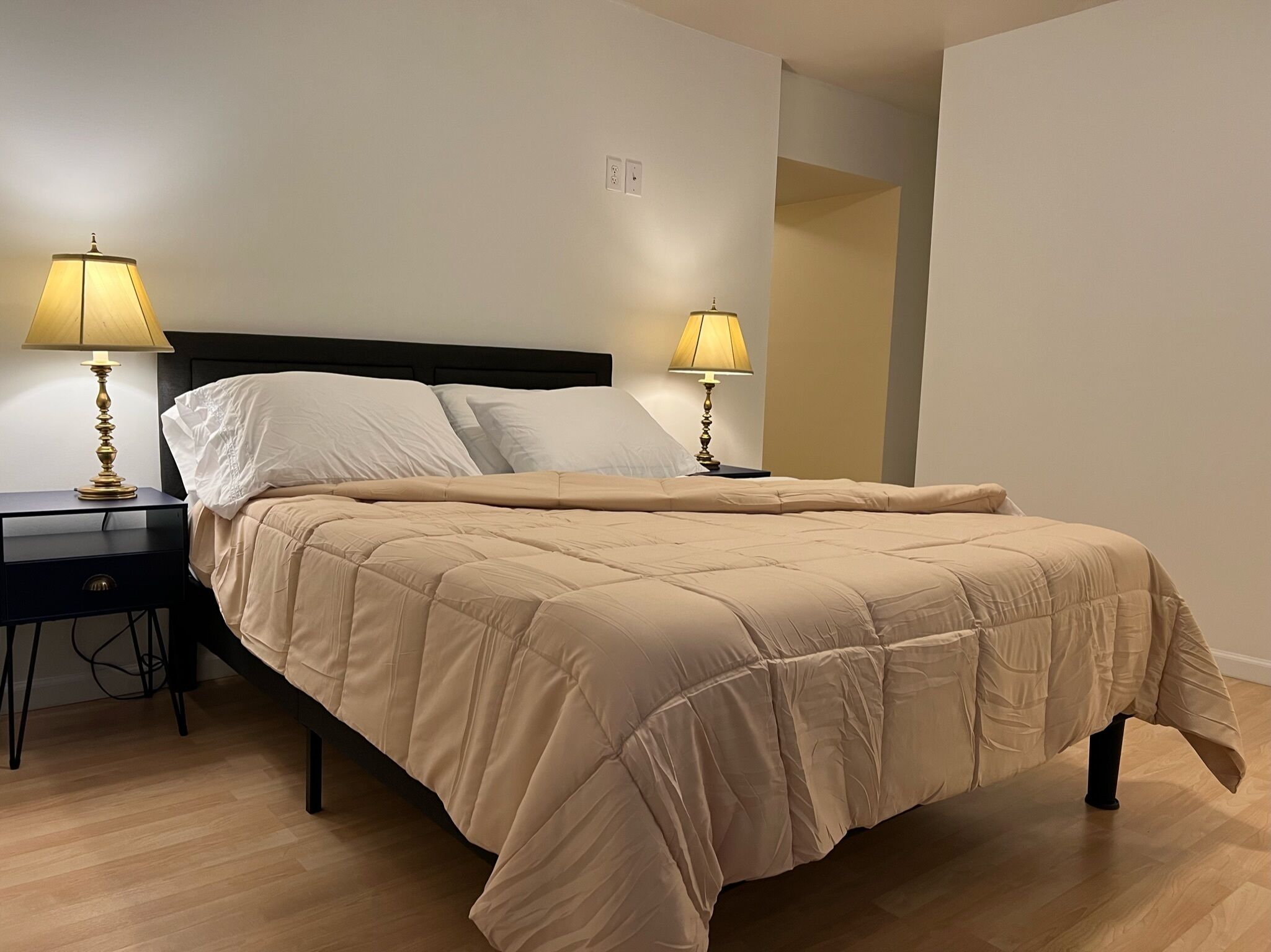 Un lit bien fait, recouvert d’une couette beige, deux tables de chevet avec des lampes et un plancher en bois.