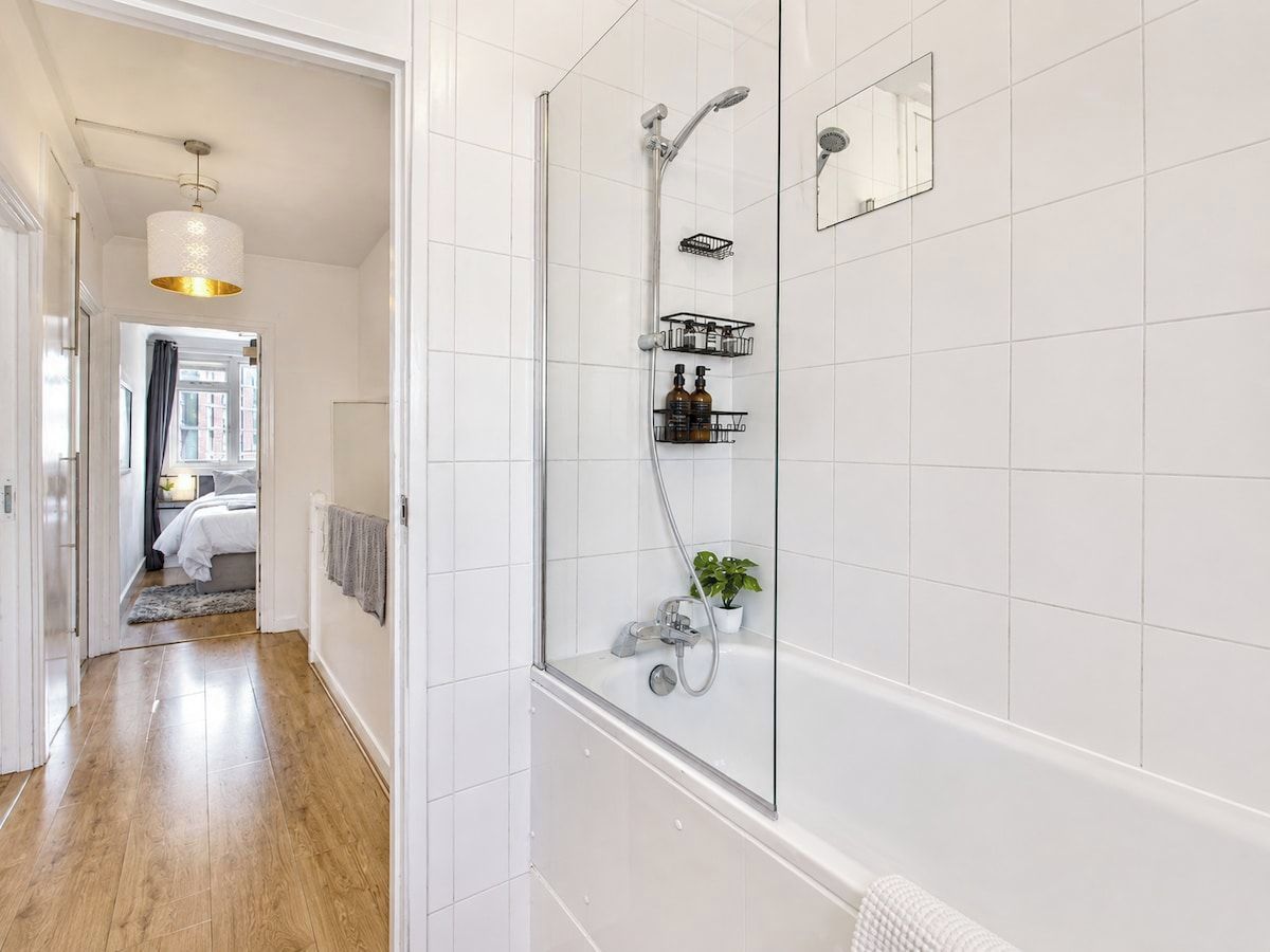 A modern bathroom with a glass-enclosed shower, white tiled walls, and a wooden floor.