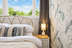 Quarto com cama, mesa de cabeceira com abajur e janela com vista para árvores.