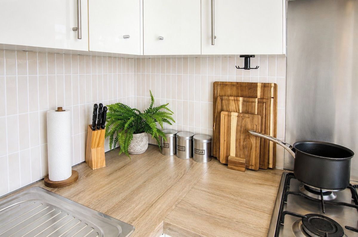 Una cocina con gabinetes blancos, una tabla de cortar de madera, una olla en la estufa y recipientes de almacenamiento.