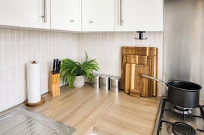 A kitchen with white cabinets, a wooden cutting board, a pot on the stove, and storage containers.