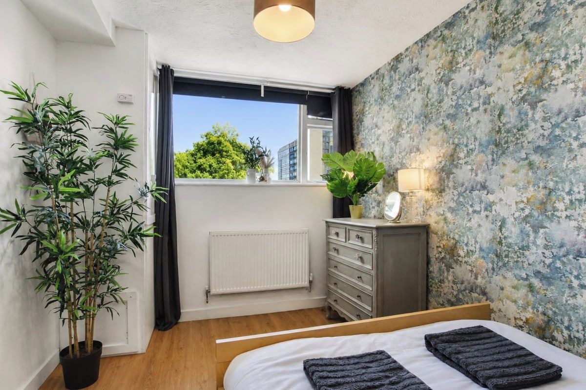 A bedroom with a bed, a dresser, a radiator, a window with a view, and a potted plant.