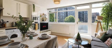 A modern kitchen with a dining area, large windows, and a cozy living space with a sofa and a small Christmas tree.
