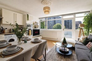 A modern kitchen with a dining area, large windows, and a cozy living space with a sofa and a small Christmas tree.