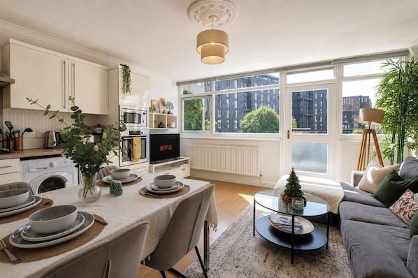 A modern kitchen with a dining area, large windows, and a cozy living space with a sofa and a small Christmas tree.