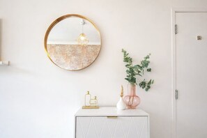 A white cabinet with a geometric pattern, a round mirror with a gold frame, and a vase with green foliage.
