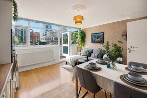 Uma sala de jantar moderna com uma mesa posta para quatro pessoas, um radiador, uma janela com vista para edifícios e uma planta pendente.