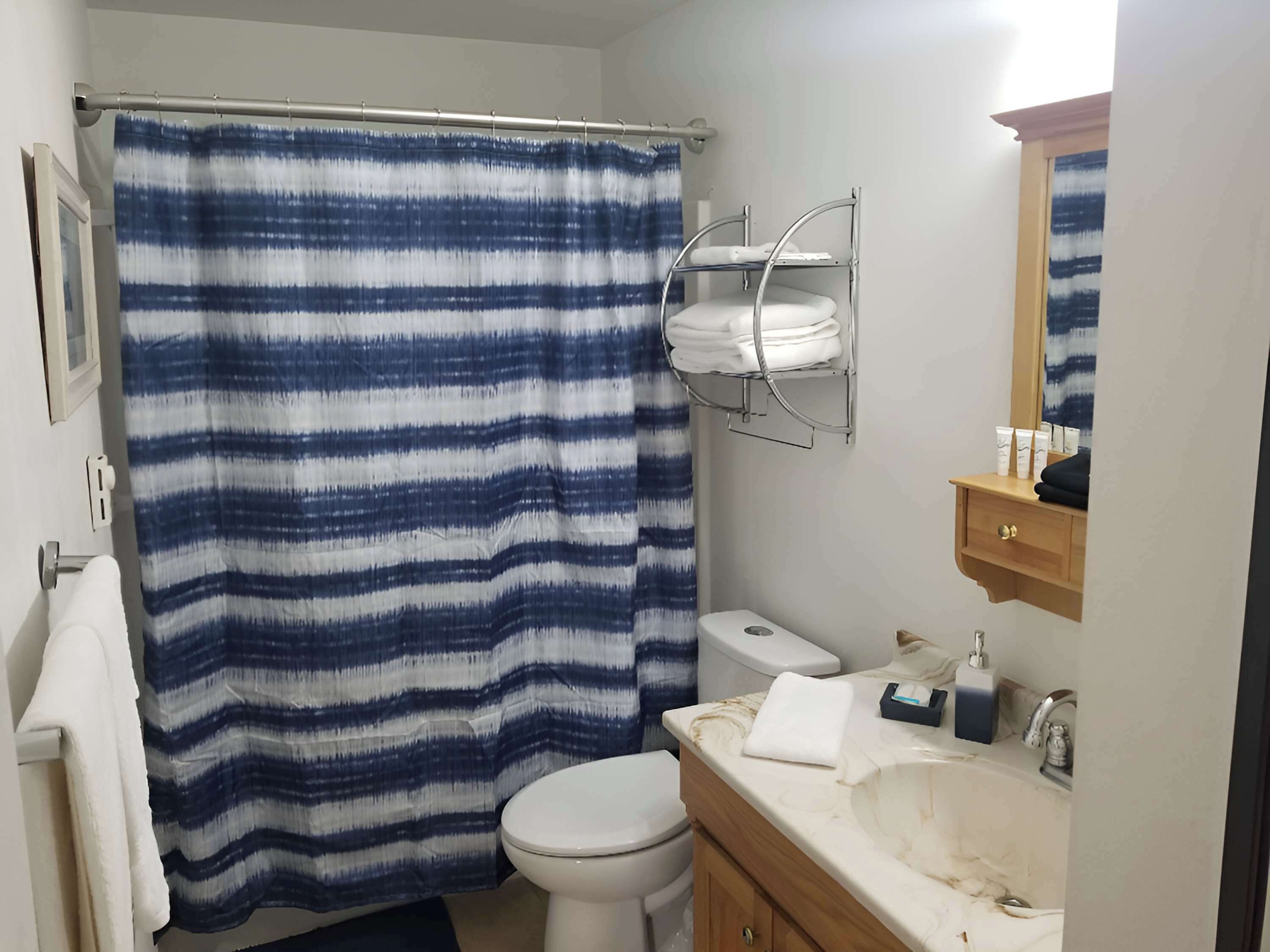 A bathroom with a striped shower curtain, a toilet, a sink with toiletries, and a mirror.