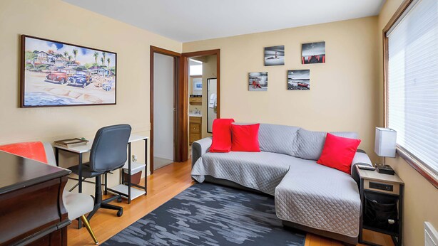 A hotel room with a bed, desk, chair, and a painting on the wall. - Full Apt with large kitchen across the street from the beach. (Blaine)