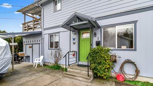 Een tweelaags huis met een groene deur, een overdekte veranda en een kleine voortuin.