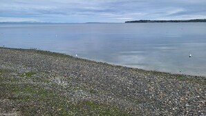 Een kiezelstrand met rustig water en land in de verte.