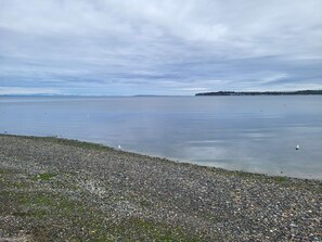 Une plage de galets avec une eau calme et une terre ferme visible au loin.
