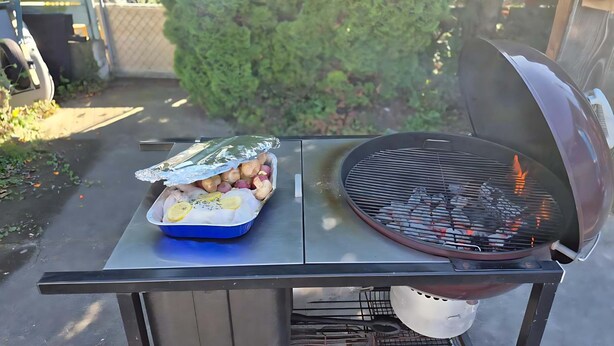 Een barbecue met een met folie ingepakte schaal eten en een grillpan met vlammen.