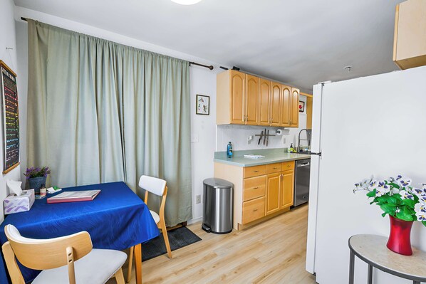 A compact kitchen with wooden cabinets, a white refrigerator, and a small dining area with a blue tablecloth.