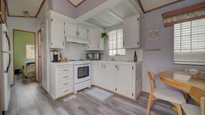 Una cocina compacta con armarios blancos, una estufa y un comedor con mesa y sillas de madera.