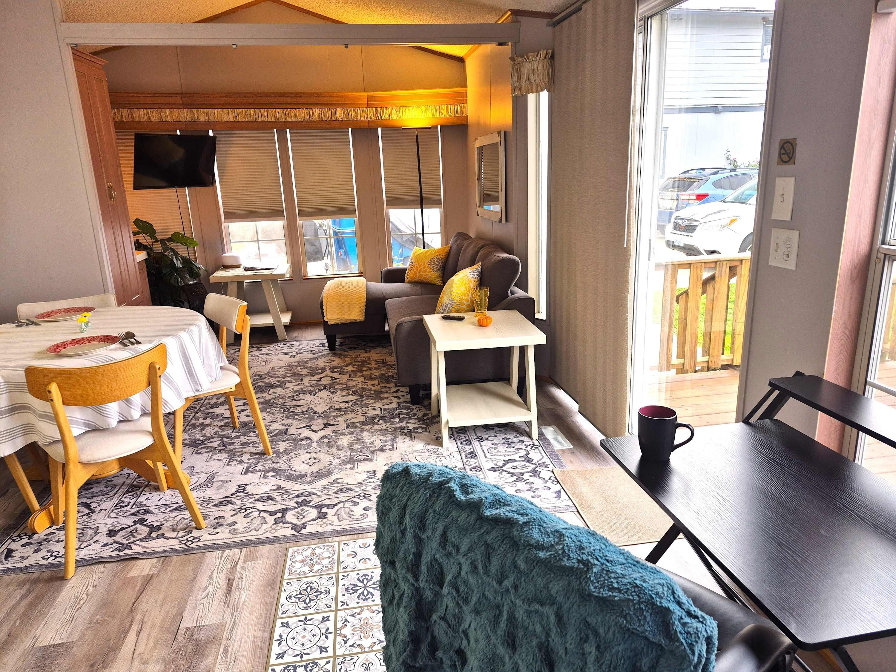 A living room with a sofa, a coffee table, a dining table with chairs, a TV, and a view of the outside.