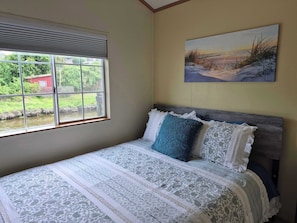 A bedroom with a large window, a bed with patterned bedding, and a painting on the wall.
