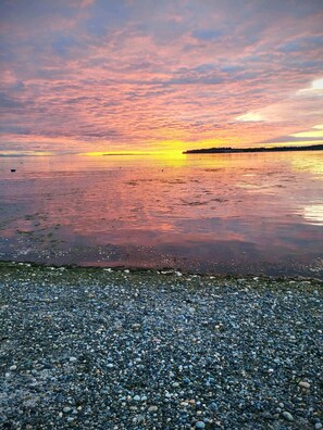 A pebbled beach with a sunset over water.