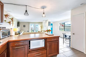 Eine moderne Küche mit Holzschränken, einer eingebauten Mikrowelle und einer großen Kochinsel. Es gibt einen Essbereich mit Tisch und Stühlen sowie ein Wohnzimmer mit Sofa und Fernseher.