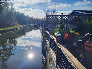 A riverside view with a wooden bridge, a building with a lattice fence, and a clear sky.