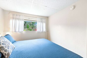 Un dormitorio con cama, cortinas, una ventana con vistas a follaje e iluminación en el techo.