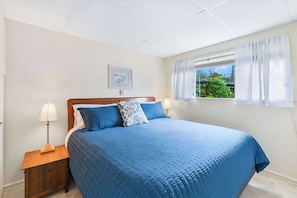 A bedroom with a large bed, two bedside tables, a window with curtains, and a picture on the wall.