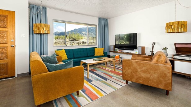 A living room with a sofa, armchairs, a coffee table, a TV, and a guitar. - Mid-Century - Views - 2 Min to Park - Retro Vibes - Game Room - Fire Pit (Twentynine Palms)