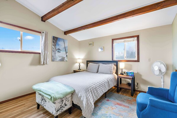 A bedroom with a bed, bedside tables, a chair, a fan, and a window.
