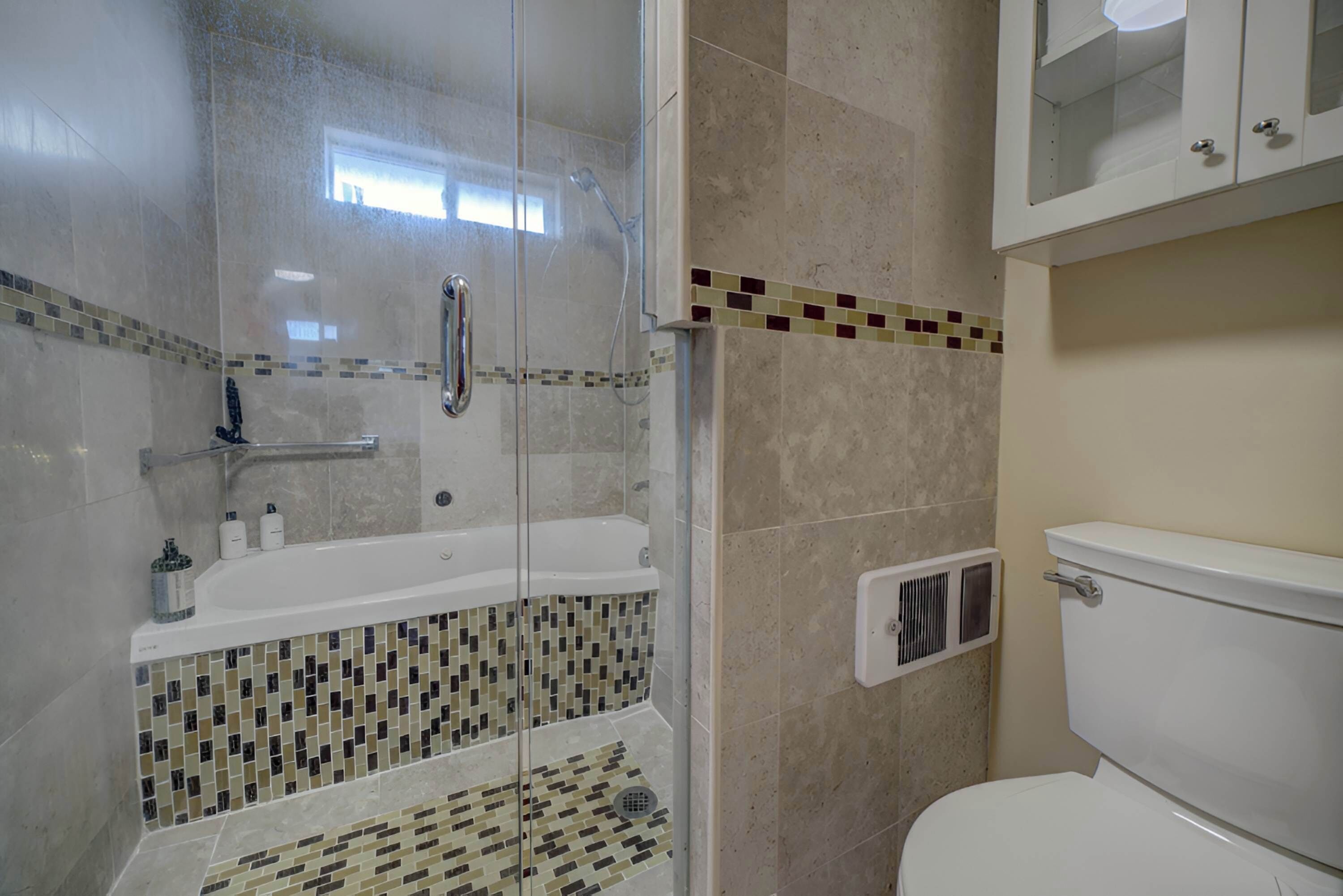 Un baño con ducha envuelta en vidrio, una bañera blanca y un inodoro.