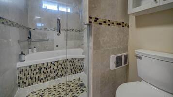 Un baño con ducha envuelta en vidrio, una bañera blanca y un inodoro.