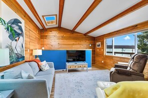 A cozy living room with a wooden interior, a blue accent wall, a fireplace, a sofa, a chair, and a large window offering a view.